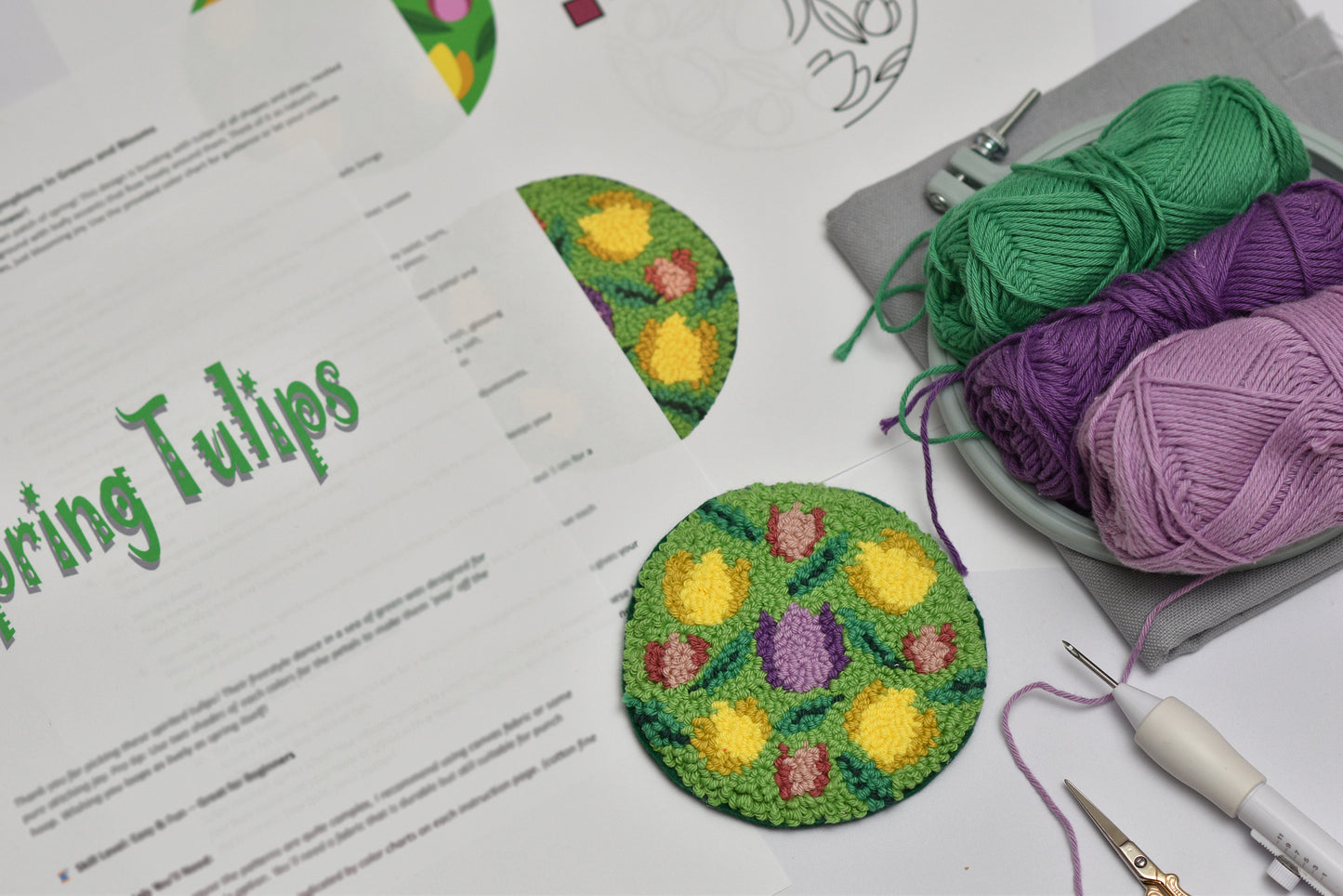 Embroidered tulip designs on paper with yarn and tools on a white surface