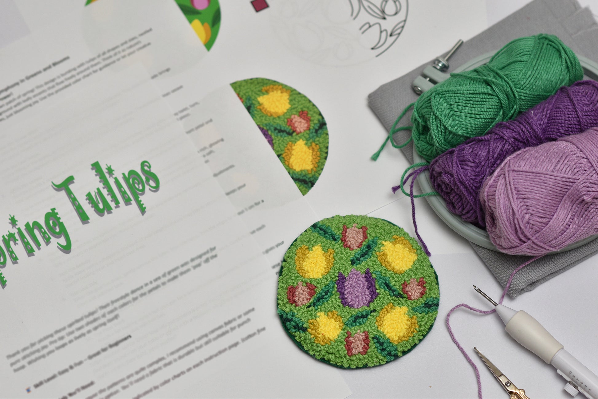 Embroidered tulip designs on paper with yarn and tools on a white surface