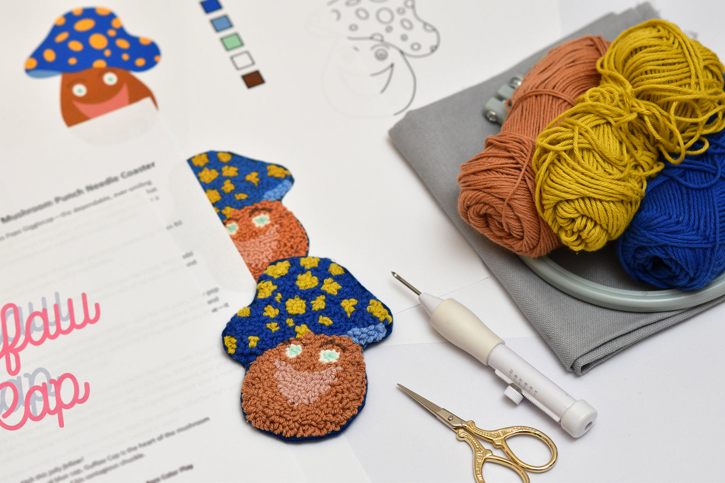 Punch needled mushroom coasters with yarn, needles, and a pattern sheet on a white surface.