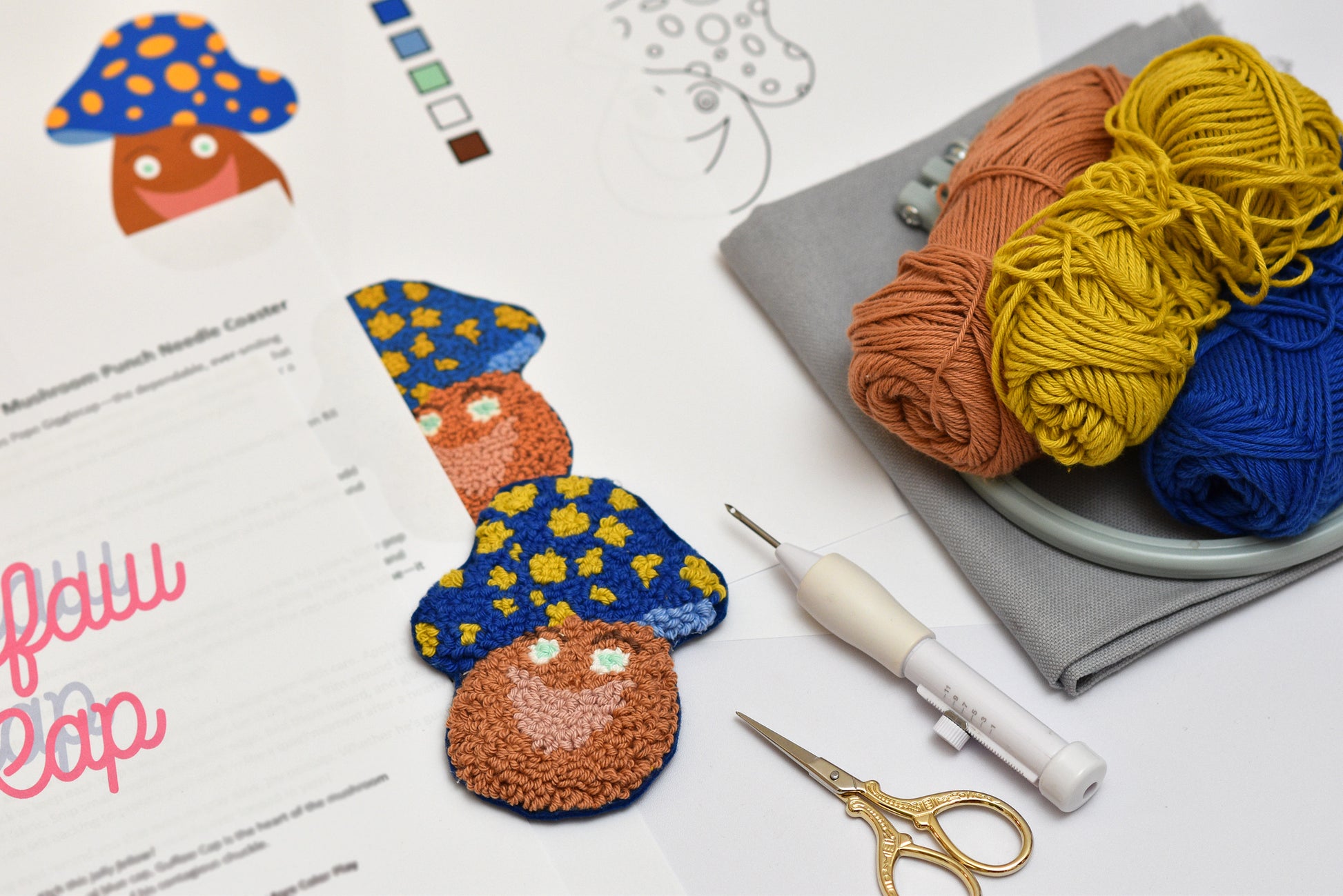 Punch needled mushroom coasters with yarn, needles, and a pattern sheet on a white surface.