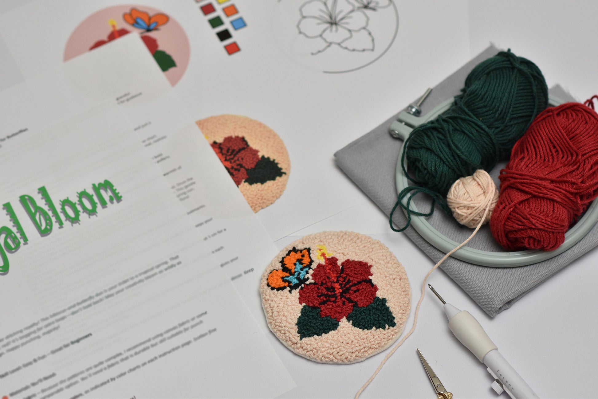 Embroidery hoop with floral design, yarn, and sewing tools on a table with 'Bloom' branding.