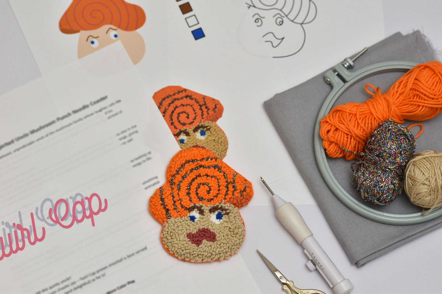 Embroidery hoop with yarn, scissors, and a completed embroidered mushroom coaster on a white surface.
