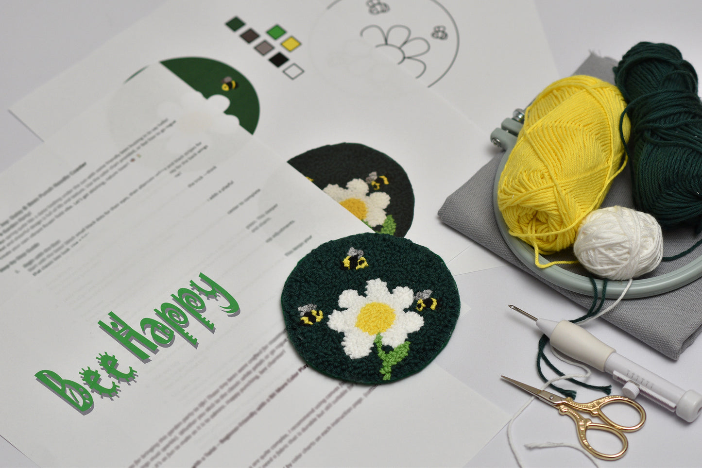 Embroidery hoop with embroidered coaster bee and daisy design, yarn, and sewing tools on a table.