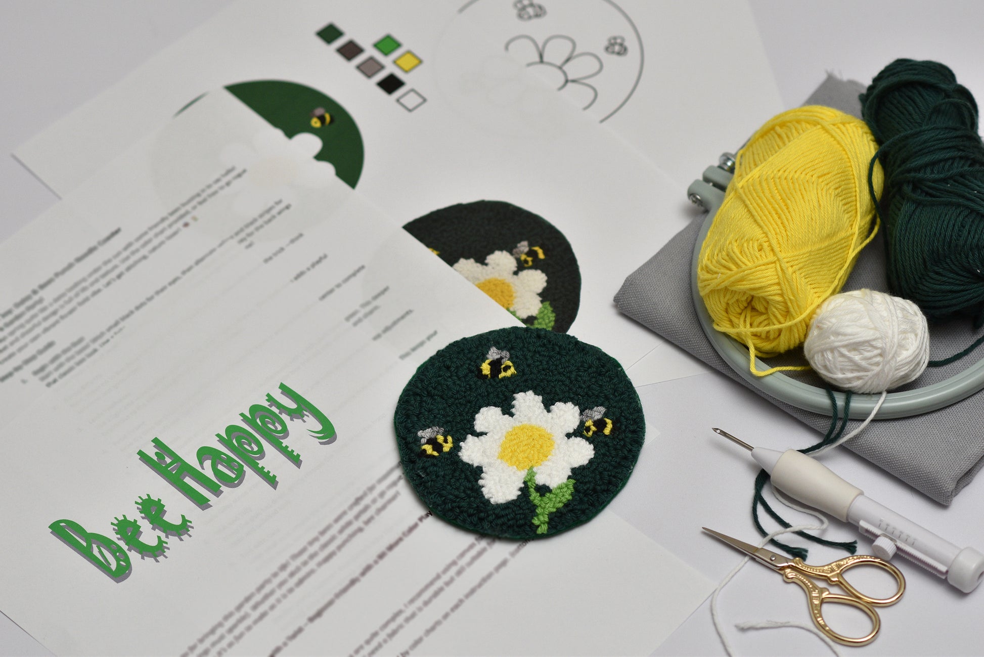 Embroidery hoop with embroidered coaster bee and daisy design, yarn, and sewing tools on a table.