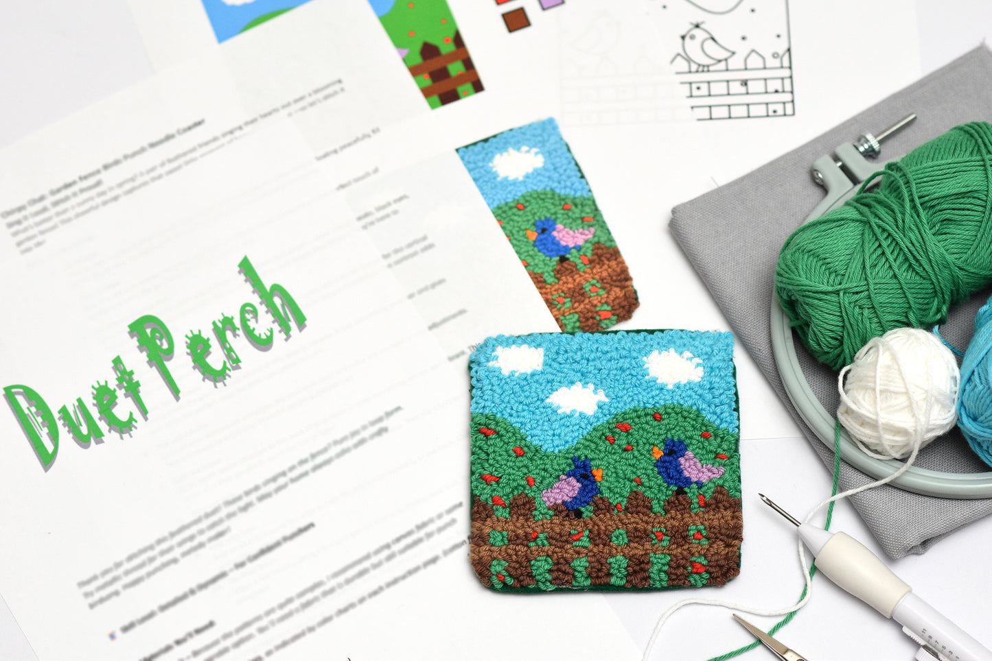 Handmade punch needle with a landscape design, yarn, and tools on a table.