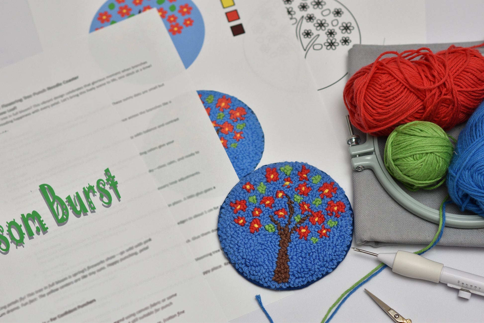 Embroidery hoop and a coaster  design featuring red flowers and green leaves, yarn, and sewing tools on a table