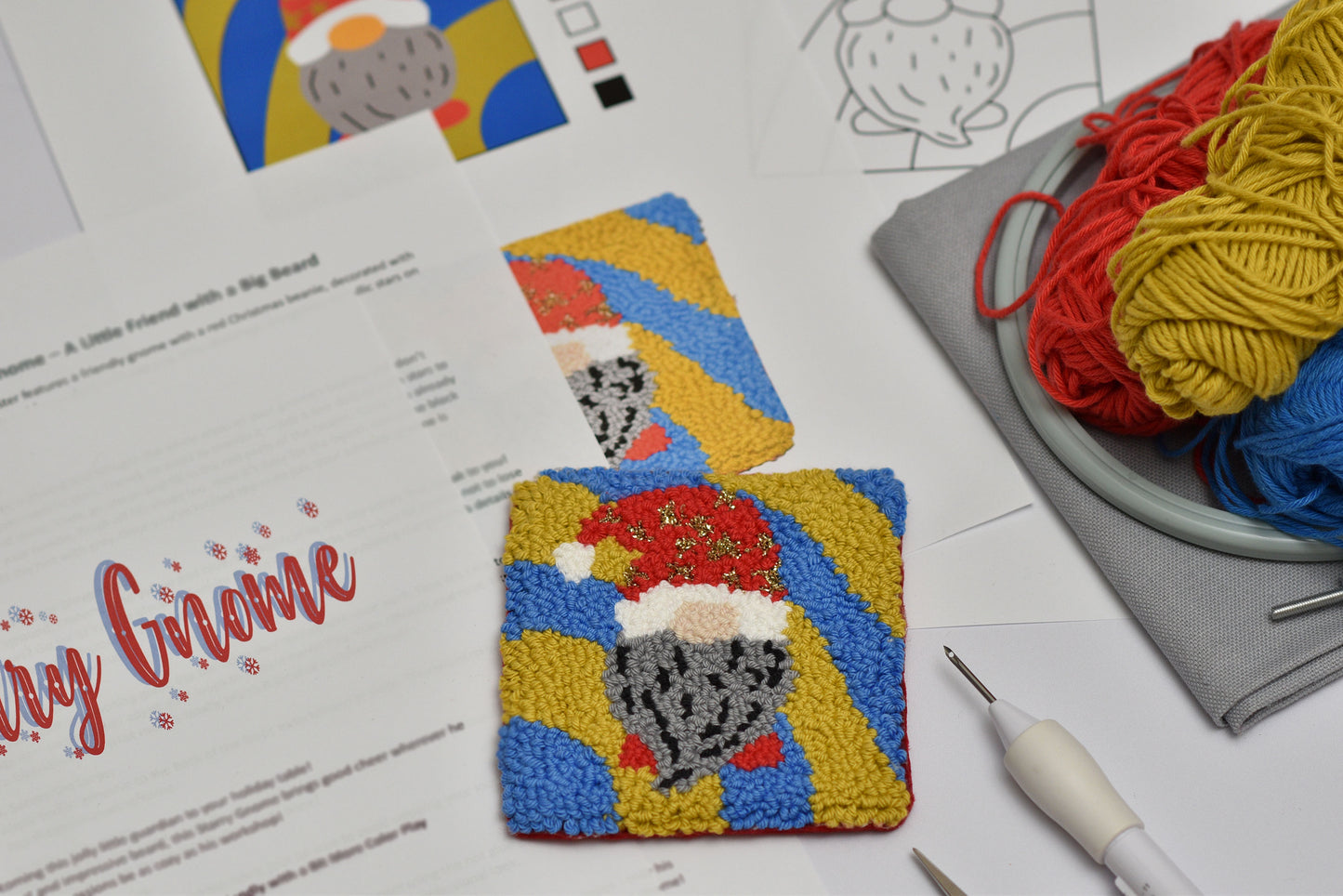 Colorful punch needled coaster with a design of a gnome on a table with yarn and tools.