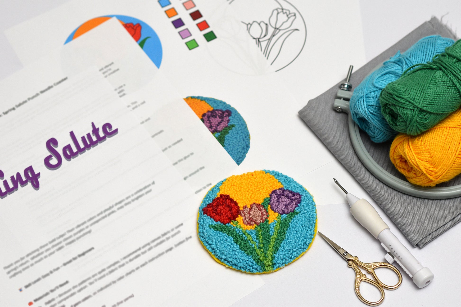 Embroidery hoop and coaster with colorful yarn, scissors, and a floral embroidery coaster design on paper.
