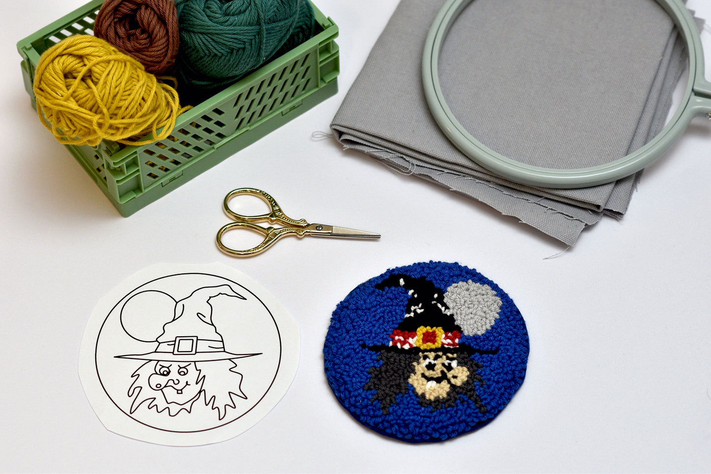 Embroidery hoop, yarn, scissors, and embroidered coaster on a white surface
