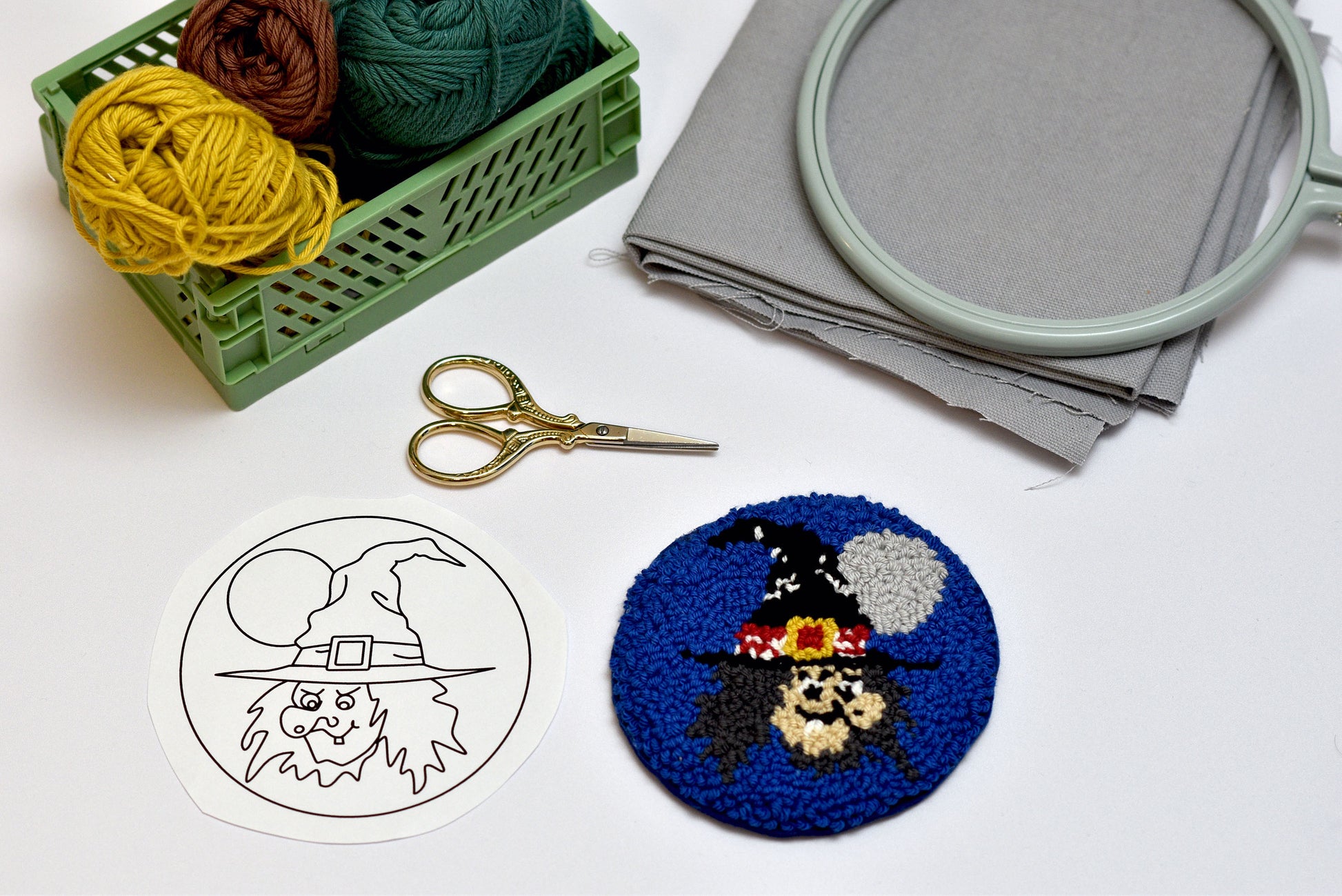 Embroidery hoop, yarn, scissors, and embroidered coaster on a white surface