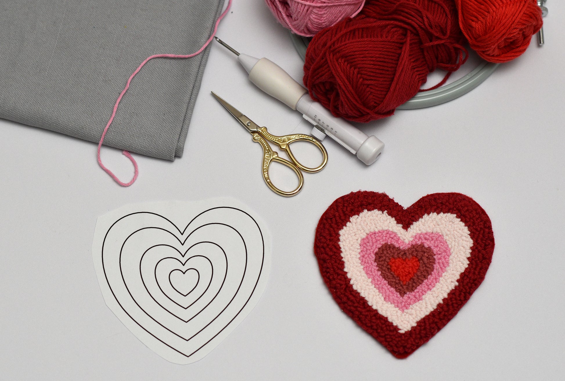 Heart-shaped craft project with yarn, scissors, and a pattern on a light surface