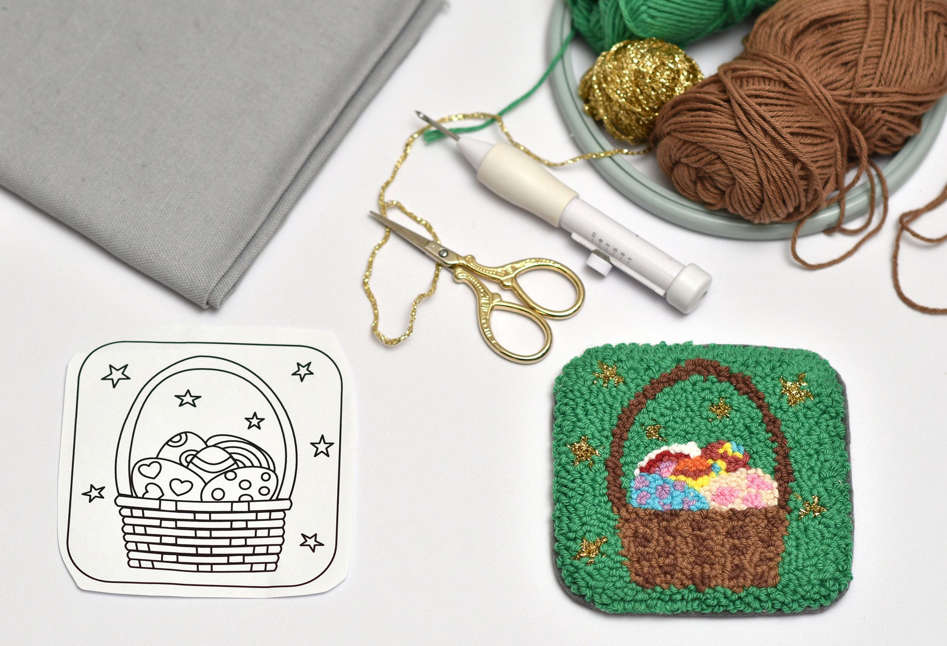 Embroidery hoop with a basket of Easter eggs design, scissors, and yarn on a white surface.