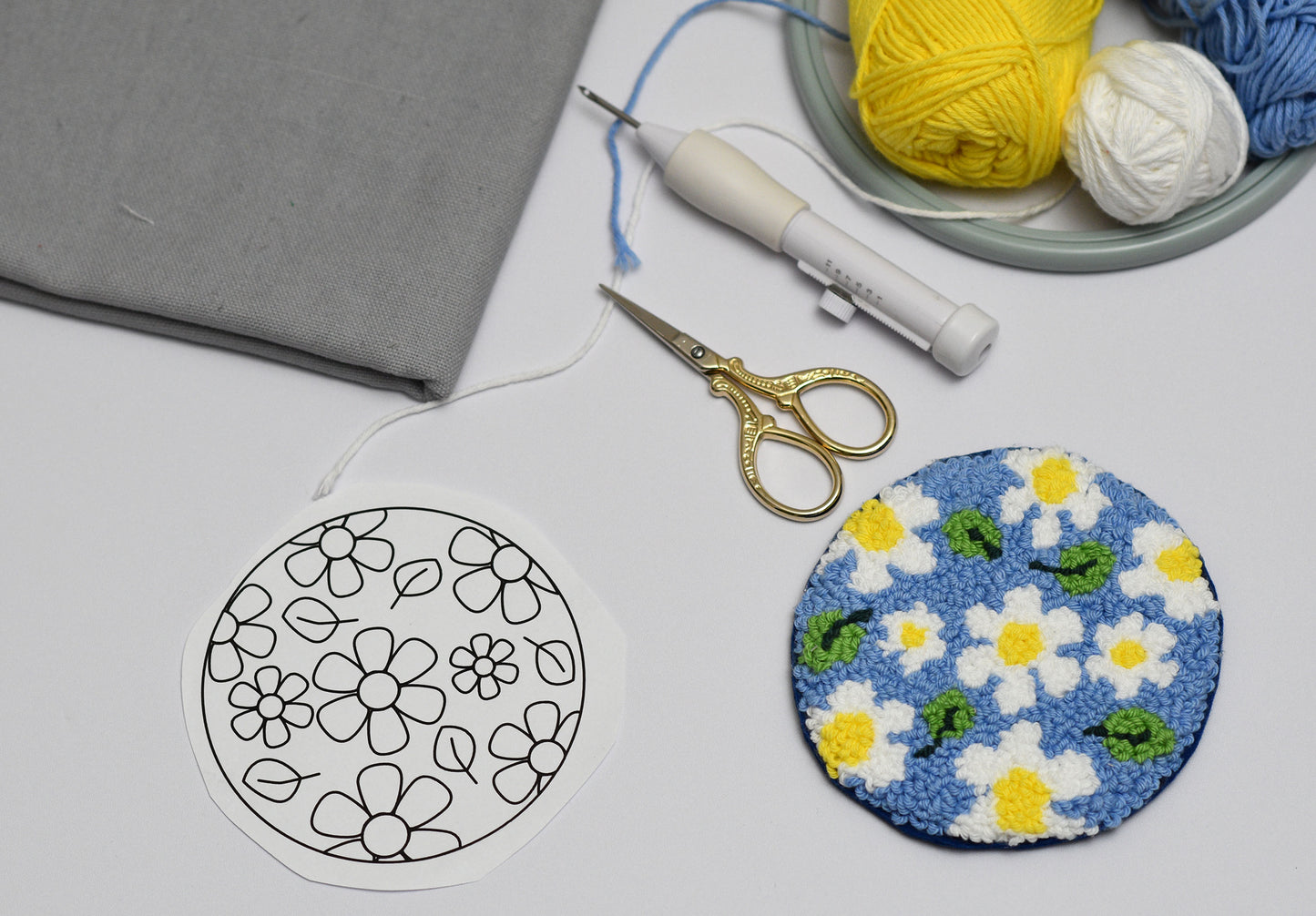 Embroidery hoop with floral daisies pattern, scissors, and yarn on a gray surface