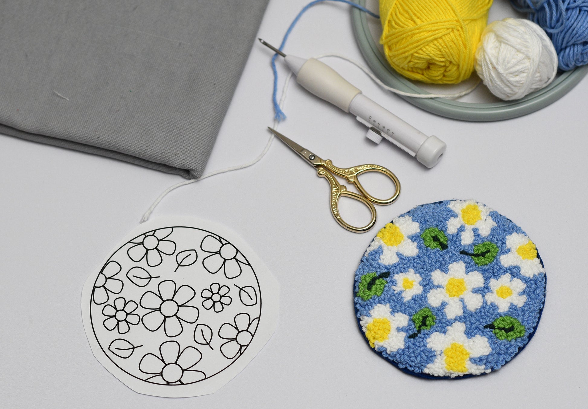 Embroidery hoop with floral daisies pattern, scissors, and yarn on a gray surface