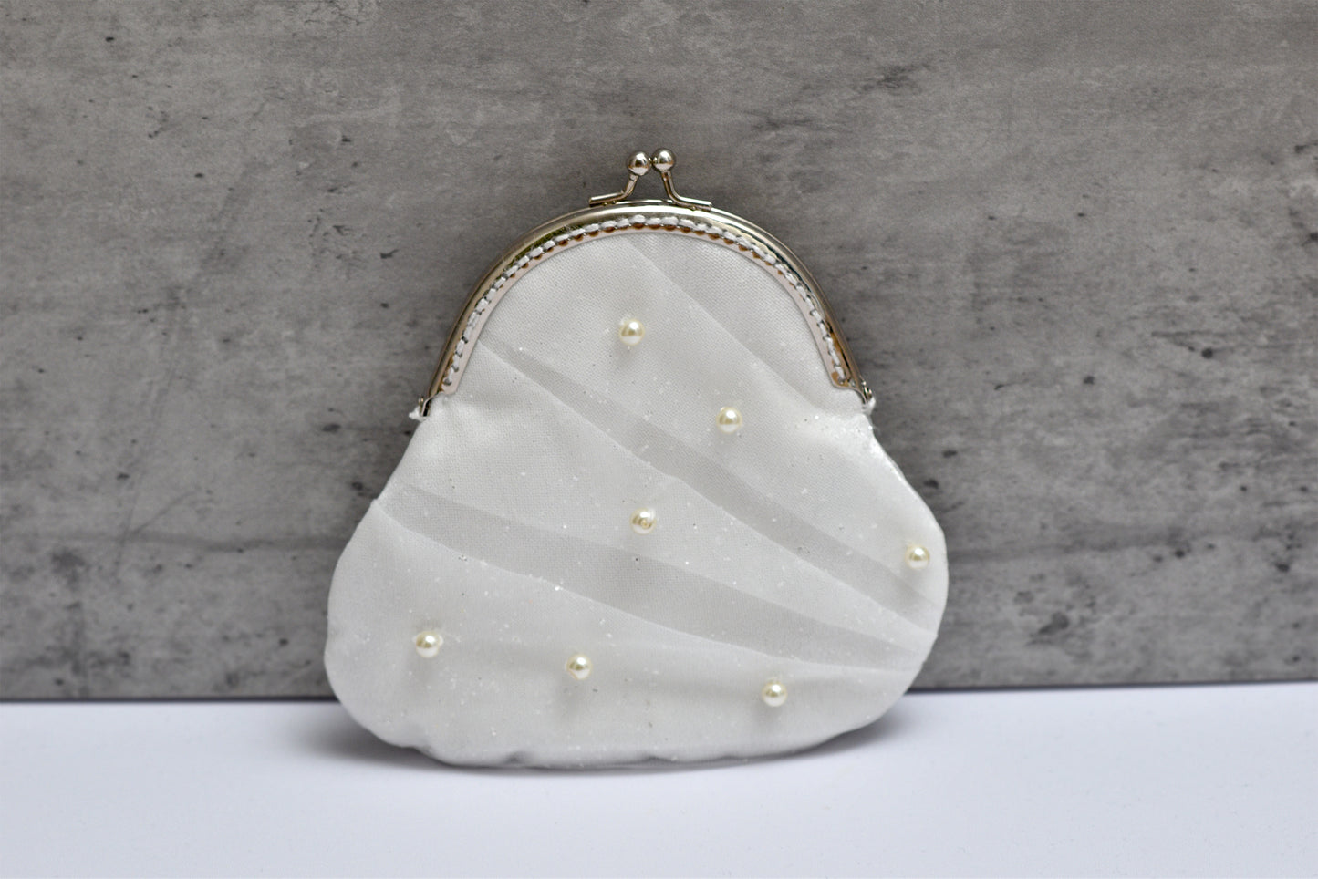 White clutch purse with pearl embellishments on a gray background