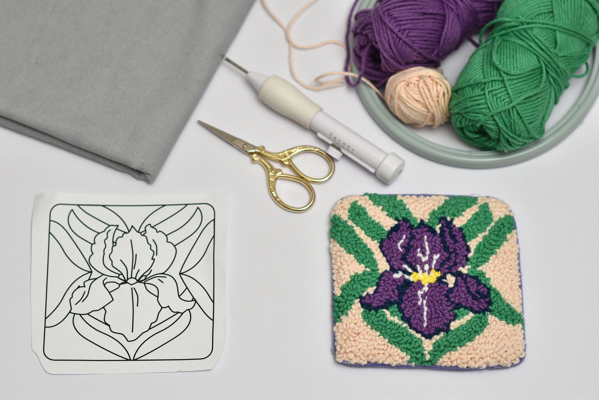 Embroidery hoop with a completed floral coaster design, yarn, scissors, and a coloring page on a table.