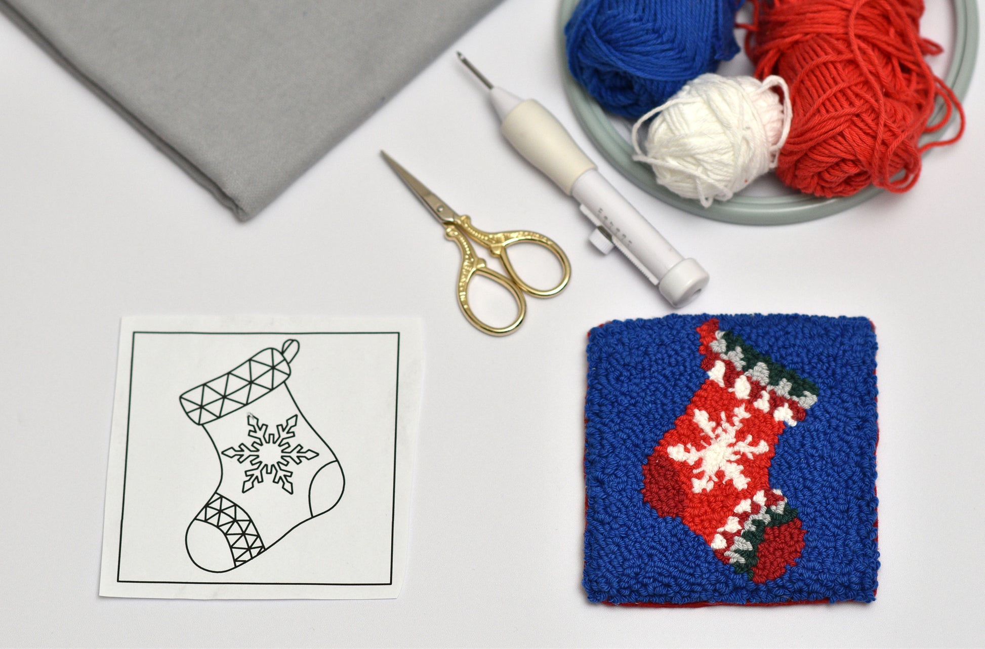 Punch needle Christmas stocking coaster with yarn, scissors, and pattern on a white surface