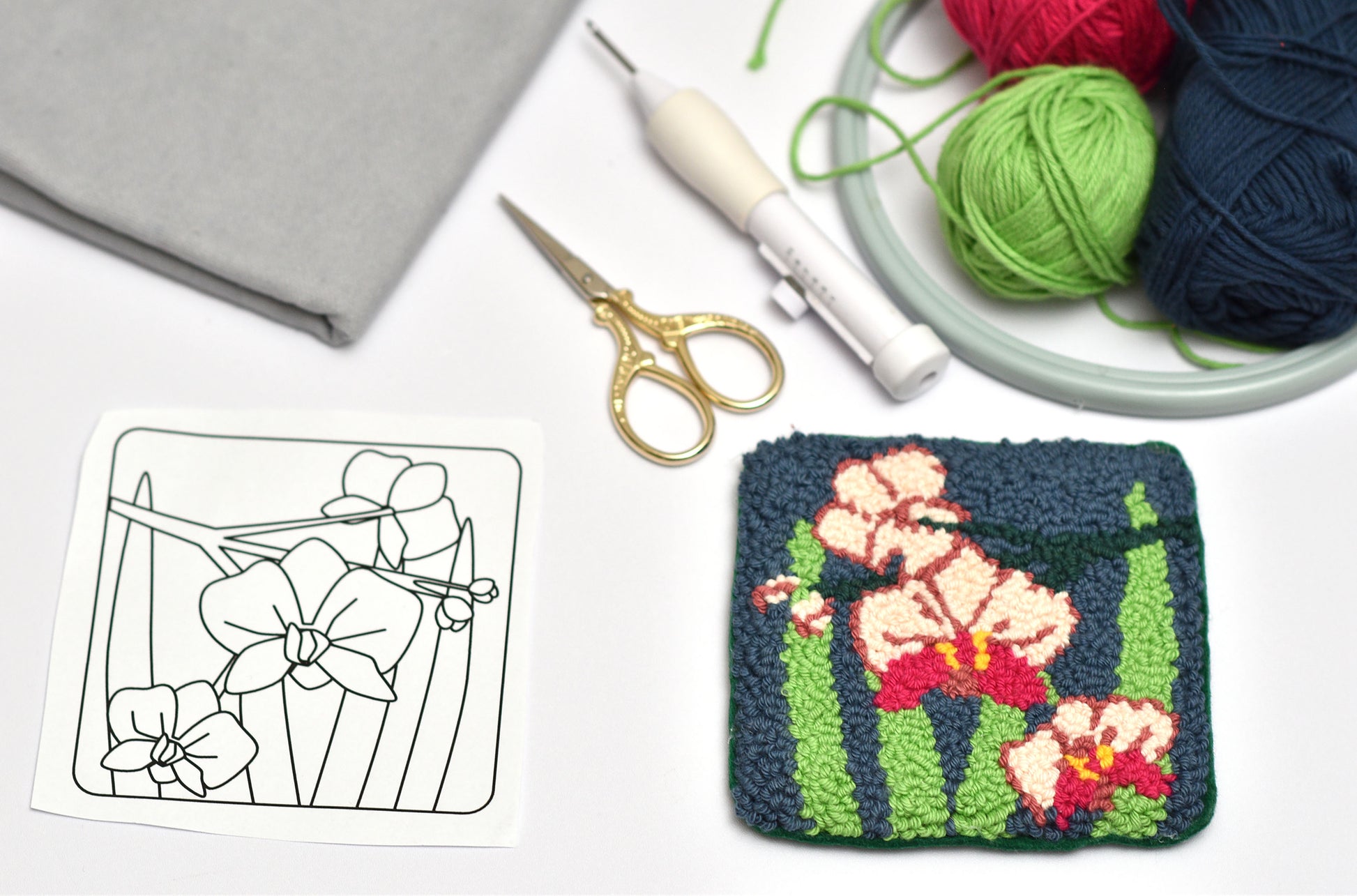 Embroidered orchid flower design on fabric with yarn, scissors, and a template.