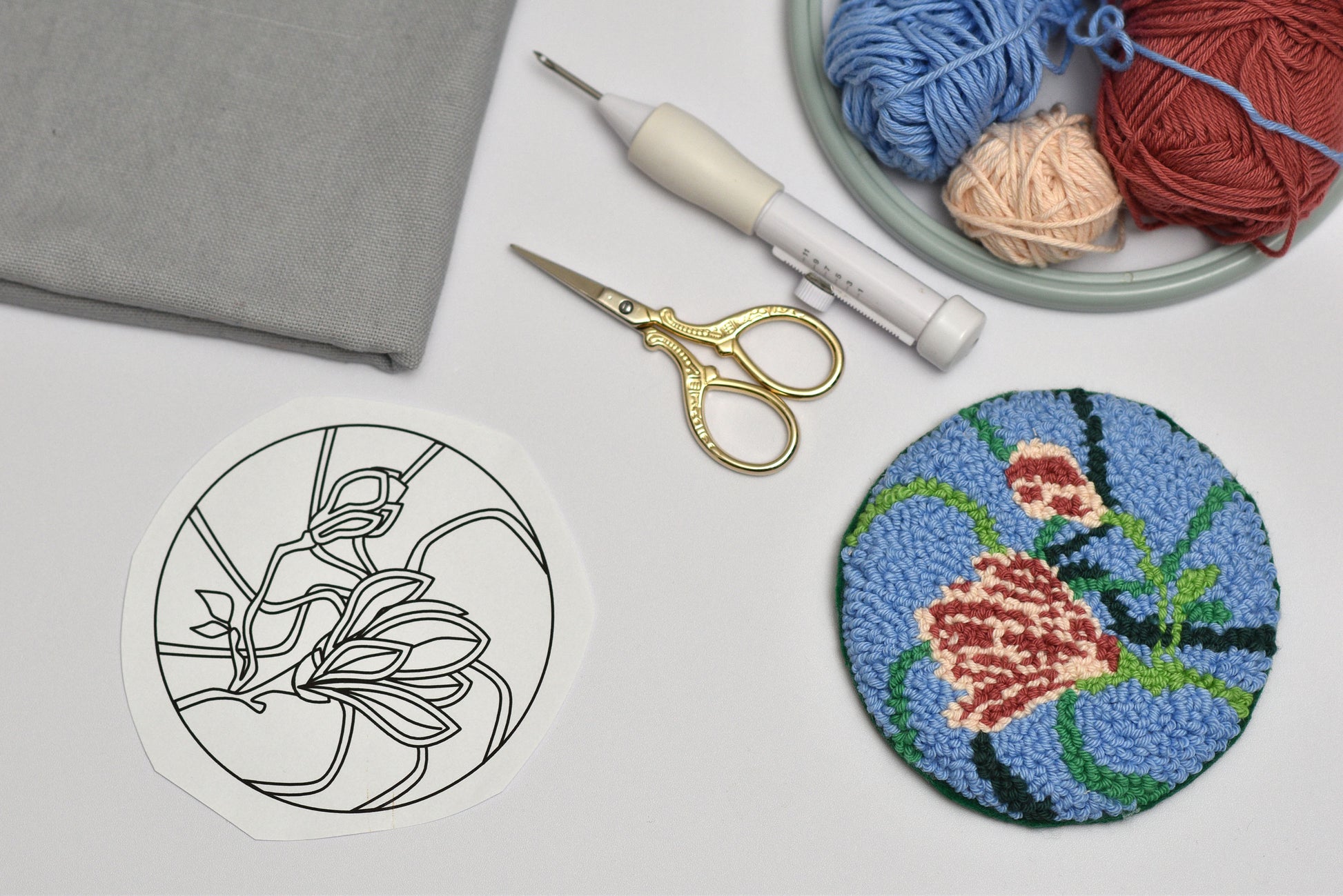 Embroidery hoop with floral magnolia design, scissors, and yarn on a white surface