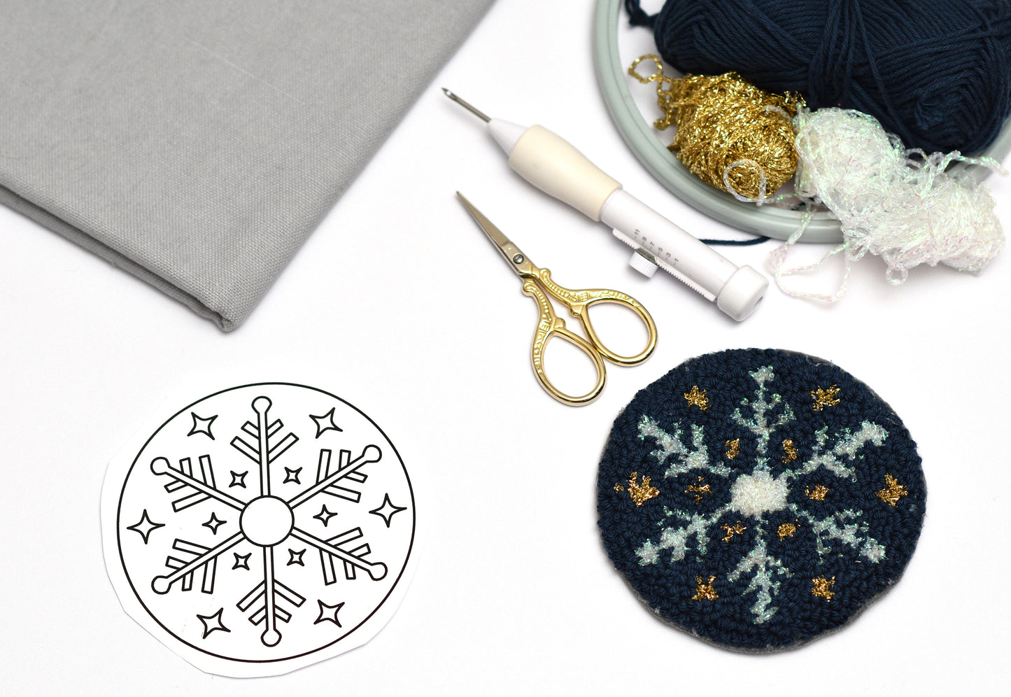 Punch needled snowflake coaster with tools and yarn on a white surface