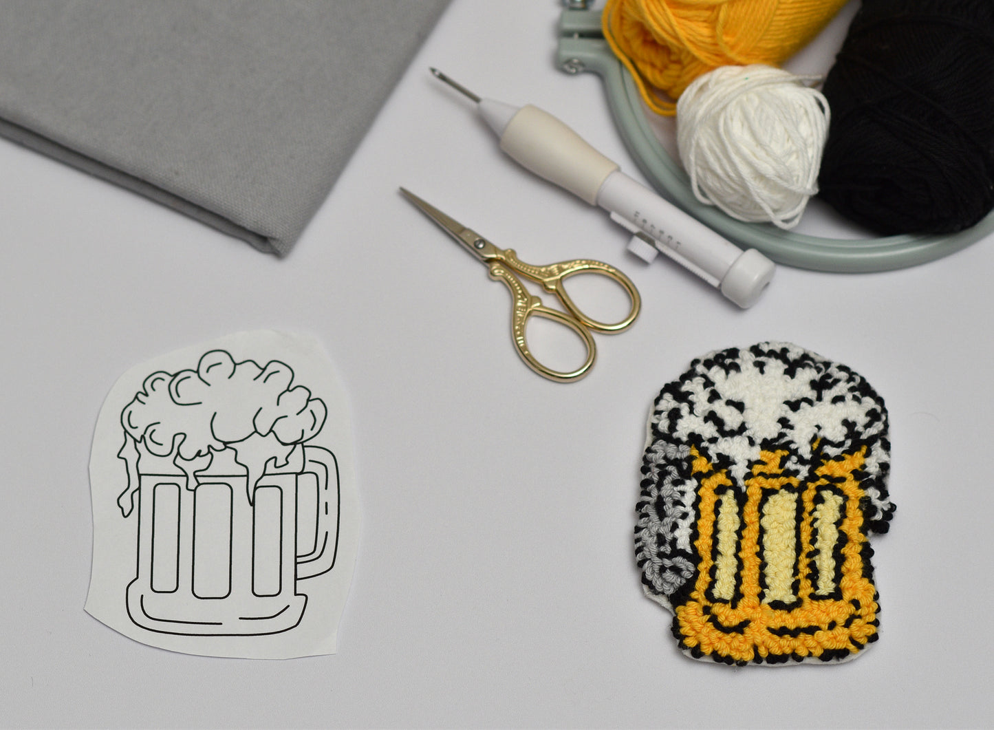 Embroidery hoop with yarn, scissors, and a completed embroidered design of a beer mug.