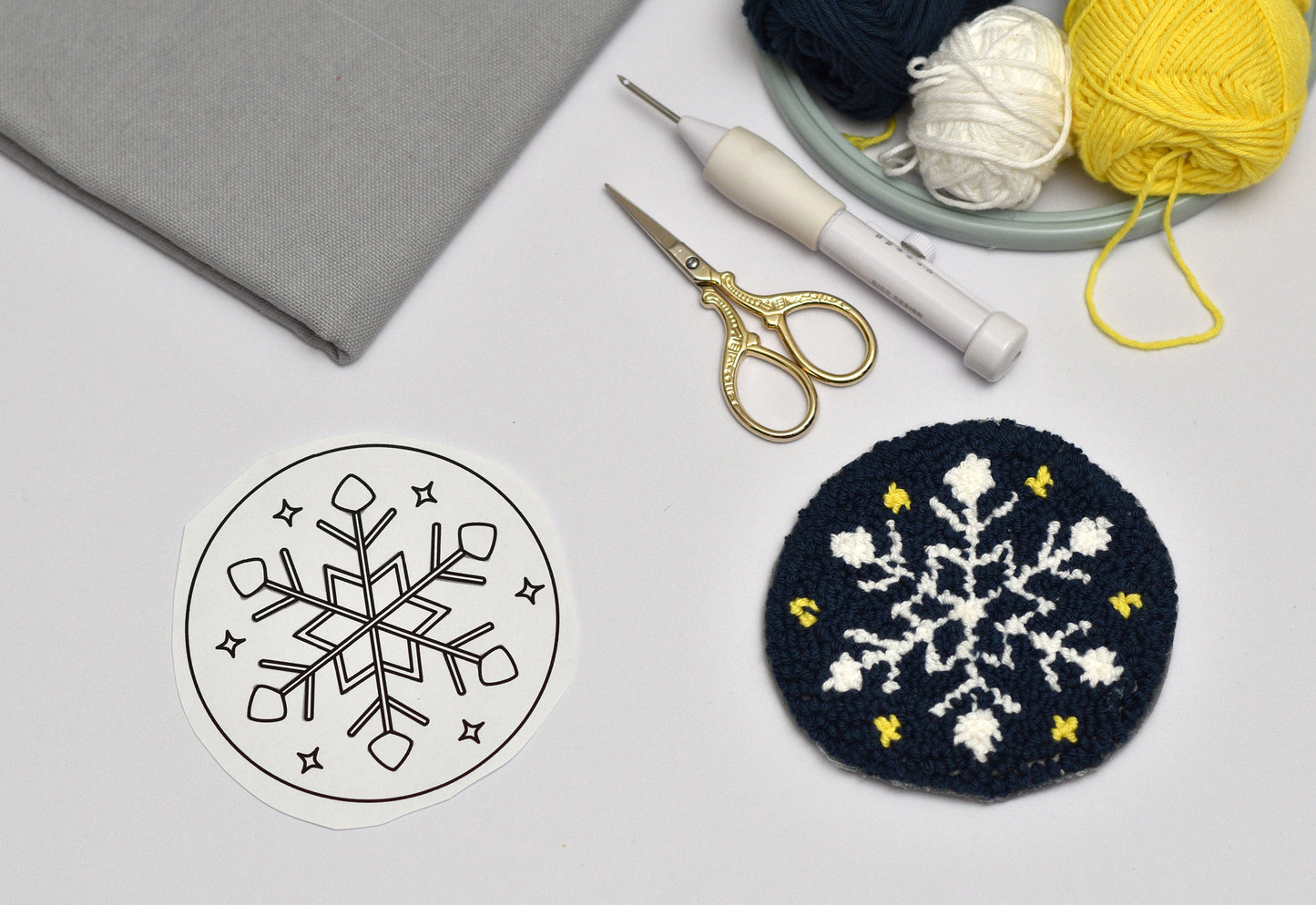 Embroidery coaster project with snowflake designs on fabric, yarn, and sewing tools.