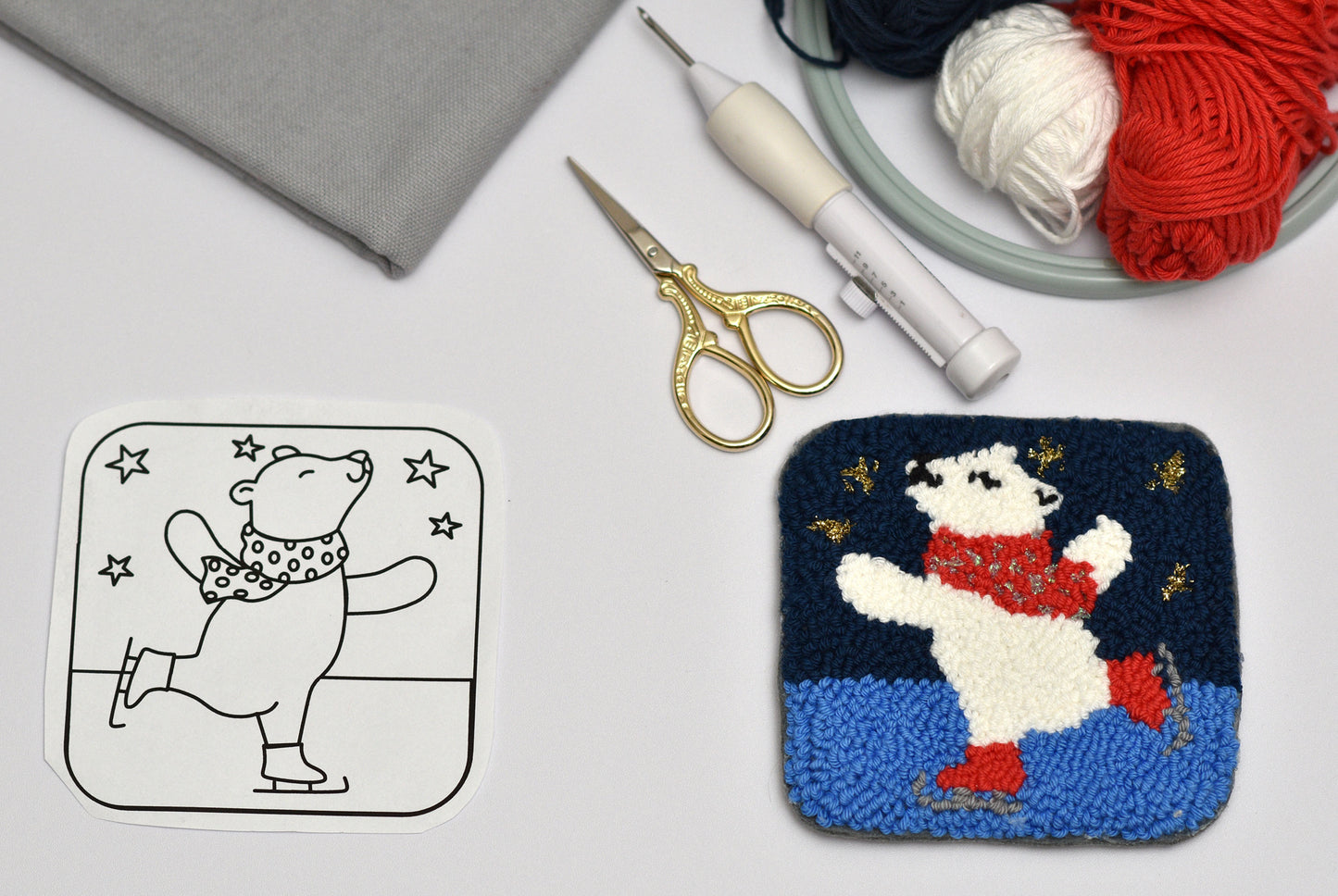 Embroidery hoop with a completed polar bear coaster design, scissors, and yarn on a table.