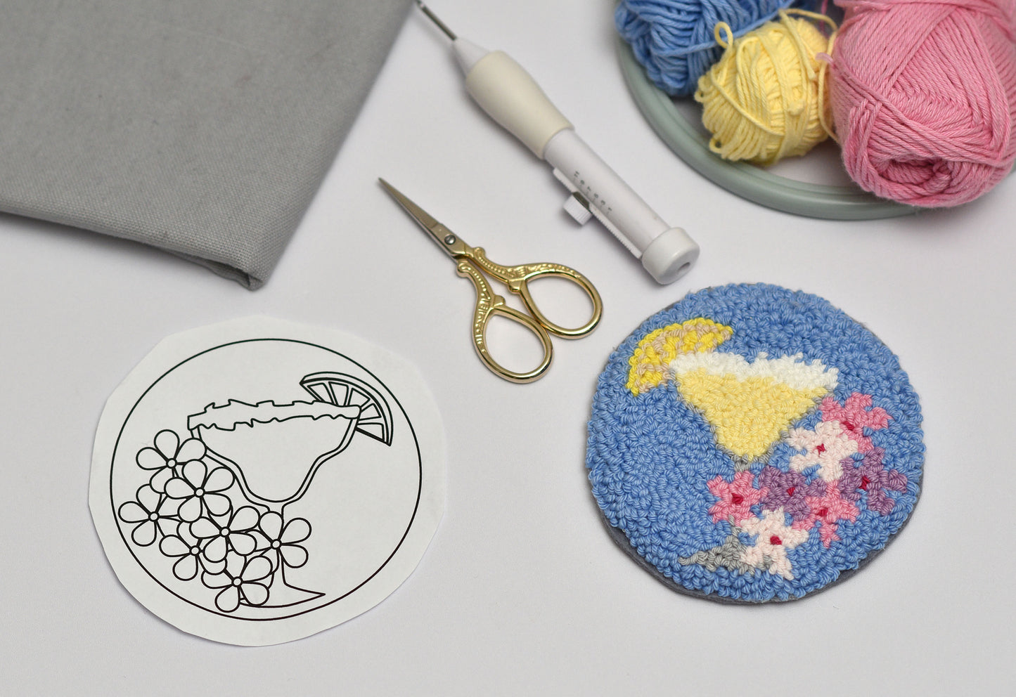 Embroidery hoop with Margarita cocktail design, scissors, and yarn on a light surface
