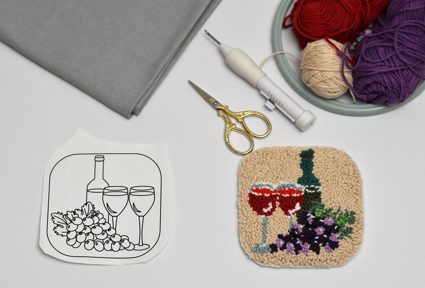 Embroidery hoop with wine-themed coaster design, scissors, and yarn on a table