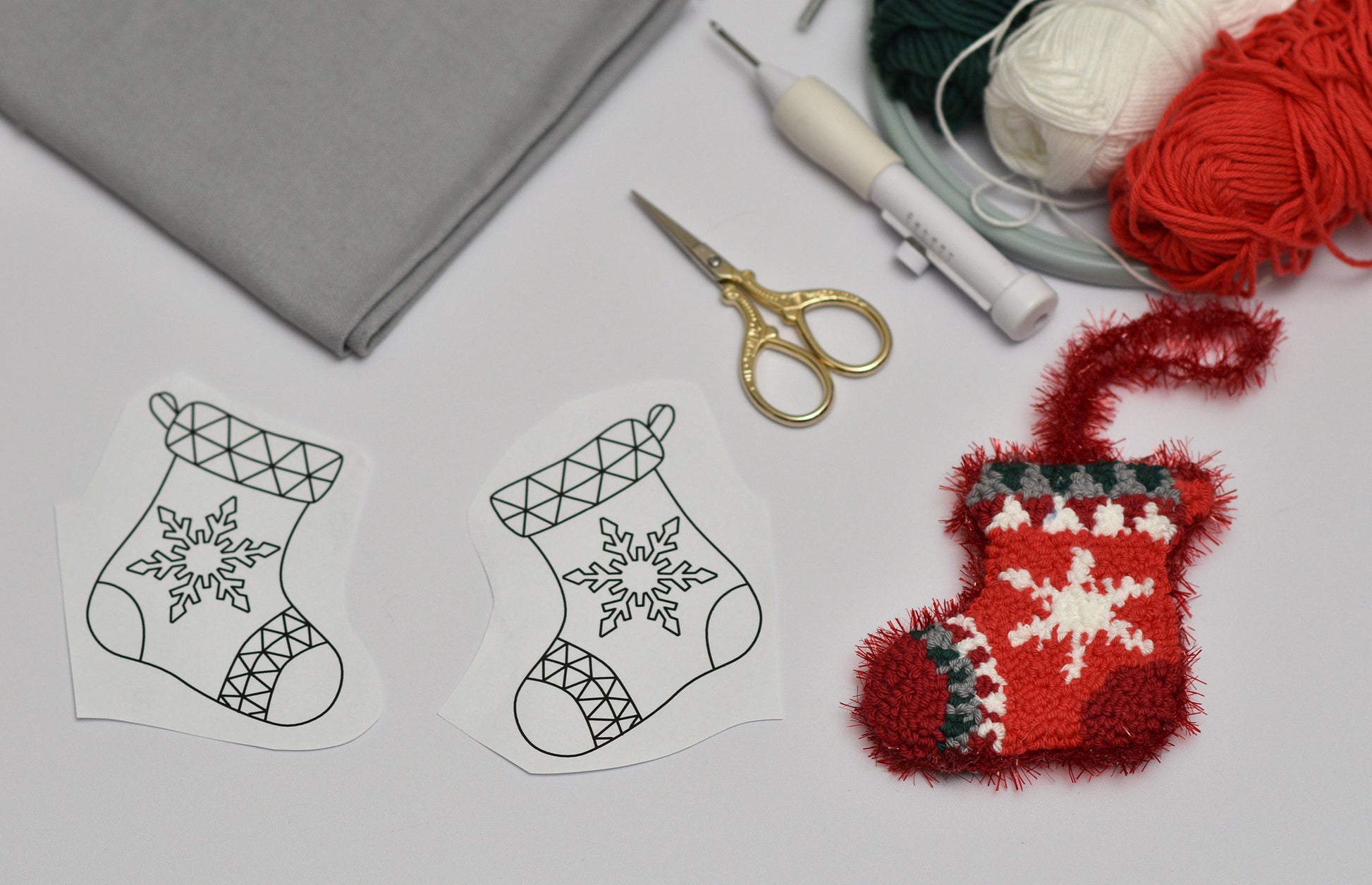 Embroidered red stocking with snowflake pattern next to paper templates and crafting supplies on a light gray surface.