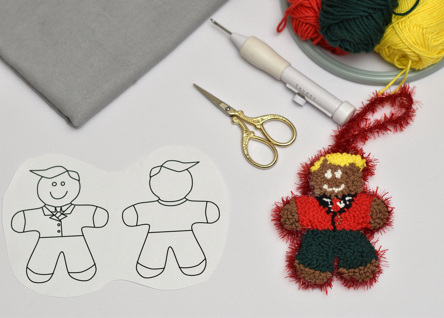 Embroidered gingerbread man ornament next to paper cutouts and crafting supplies on a table