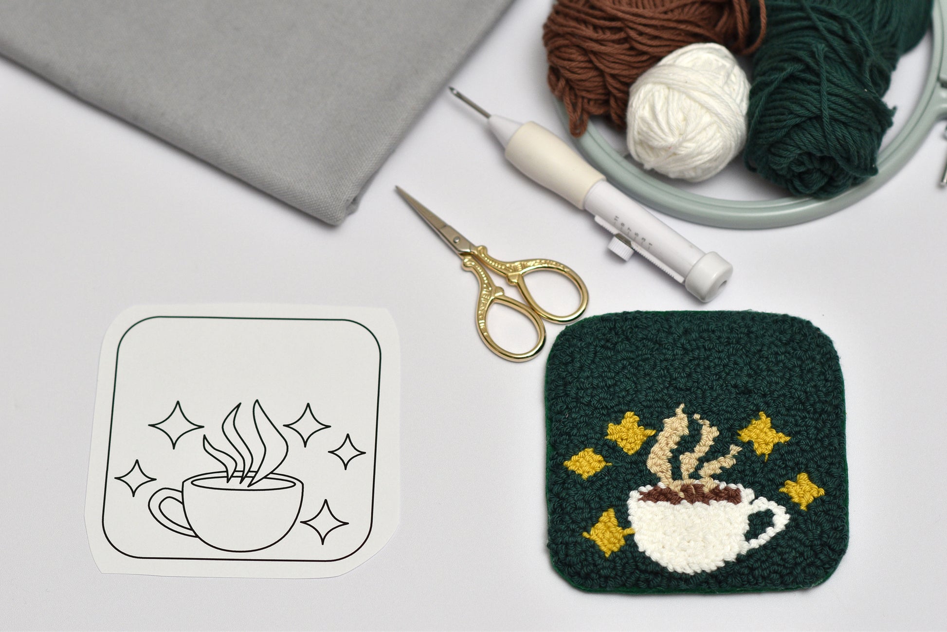 Embroidery hoop with yarn, scissors, and embroidered coaster with Coffee cup design on a light gray background