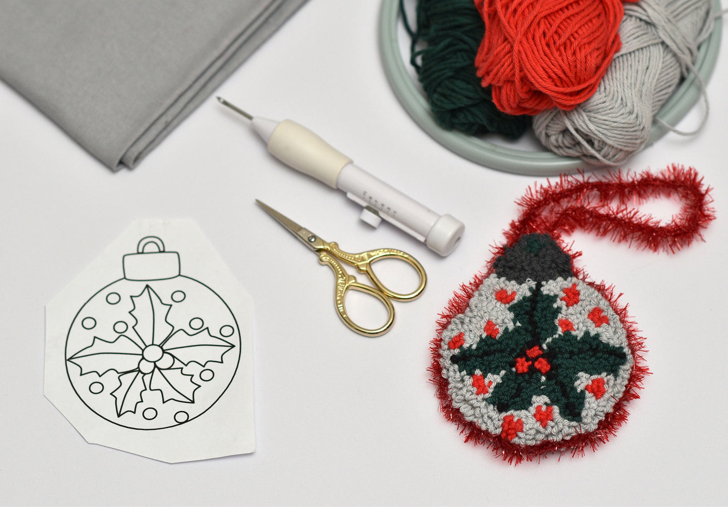 Crafting materials including a yarn ball, scissors, and a embroidered Christmas ornament on a white surface.