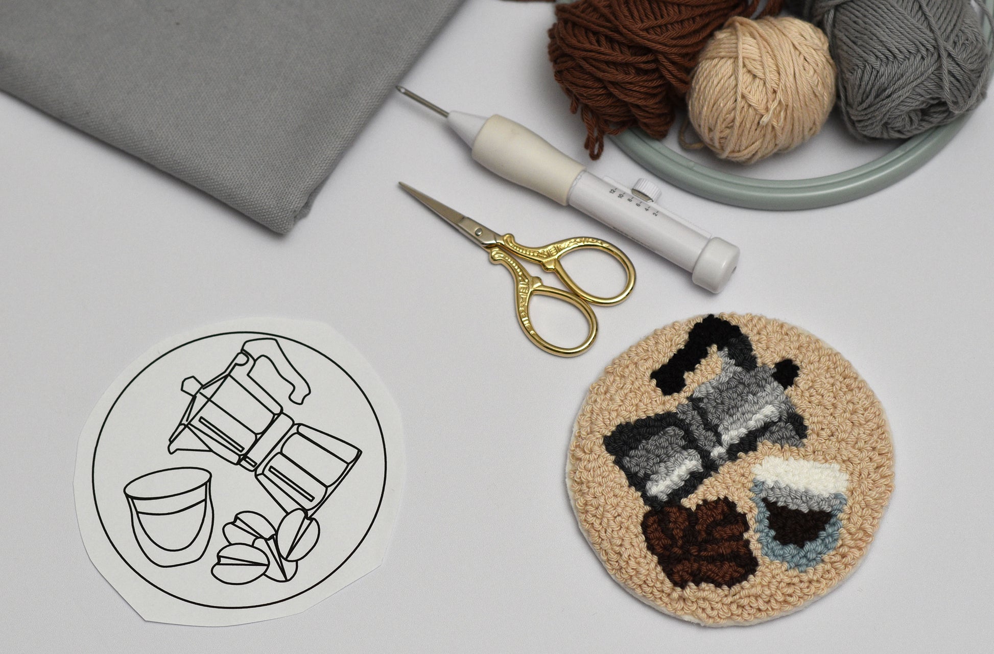 Round punch needle coaster with Espresso coffee-themed design, scissors, and yarn on a light gray background