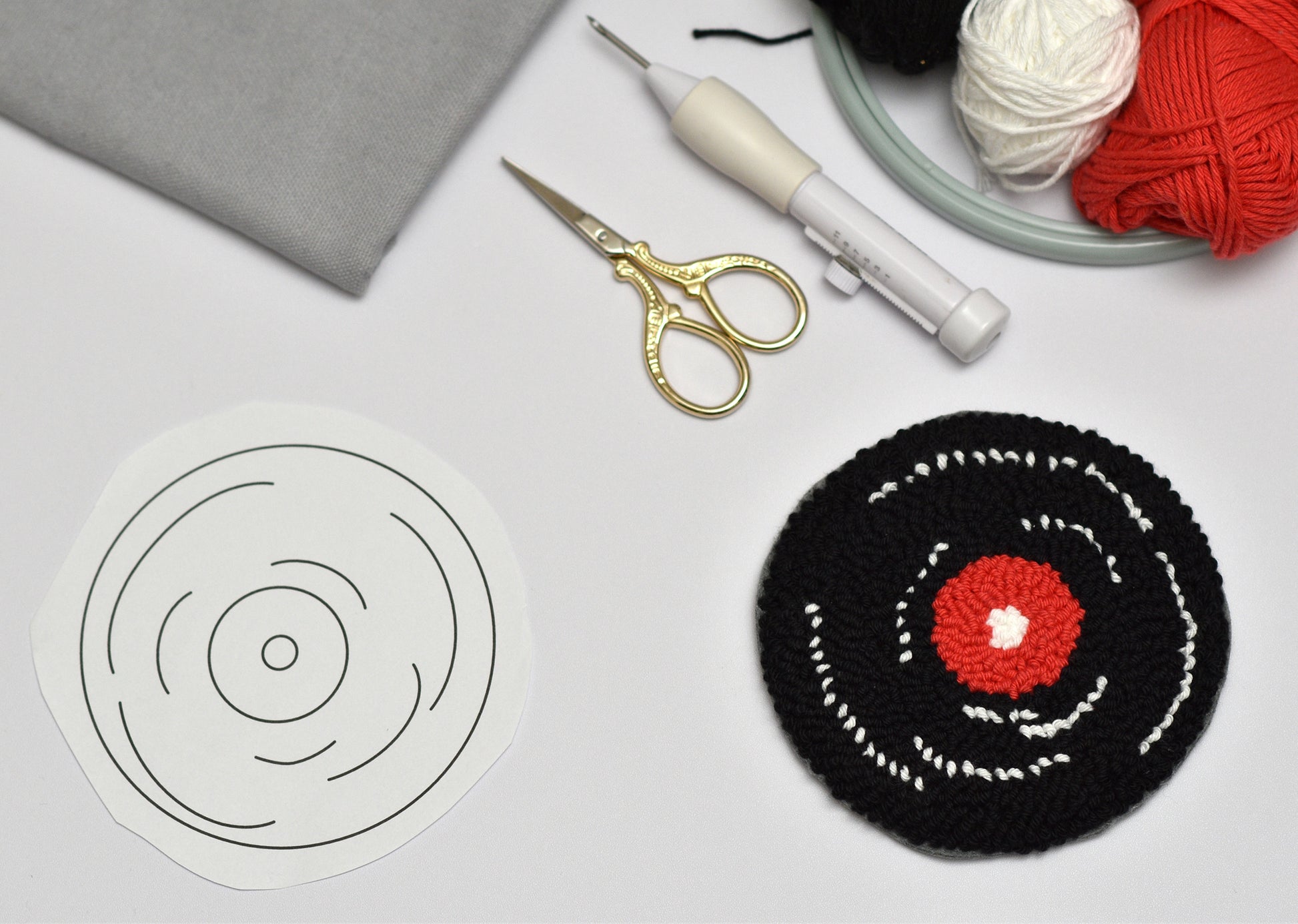 Embroidery pattern board with completed punch needle coaster, scissors, and yarn on a gray surface