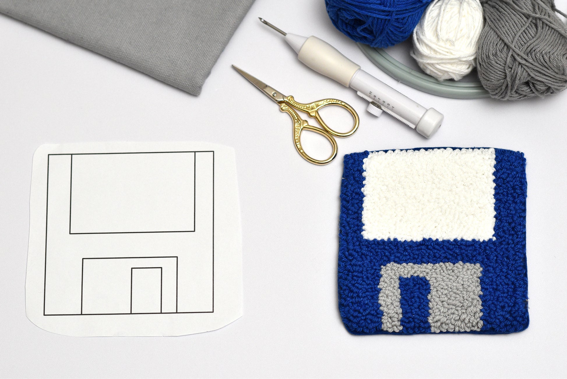 Embroidered floppy disc coaster pattern on a white surface with yarn, scissors, and a pen.