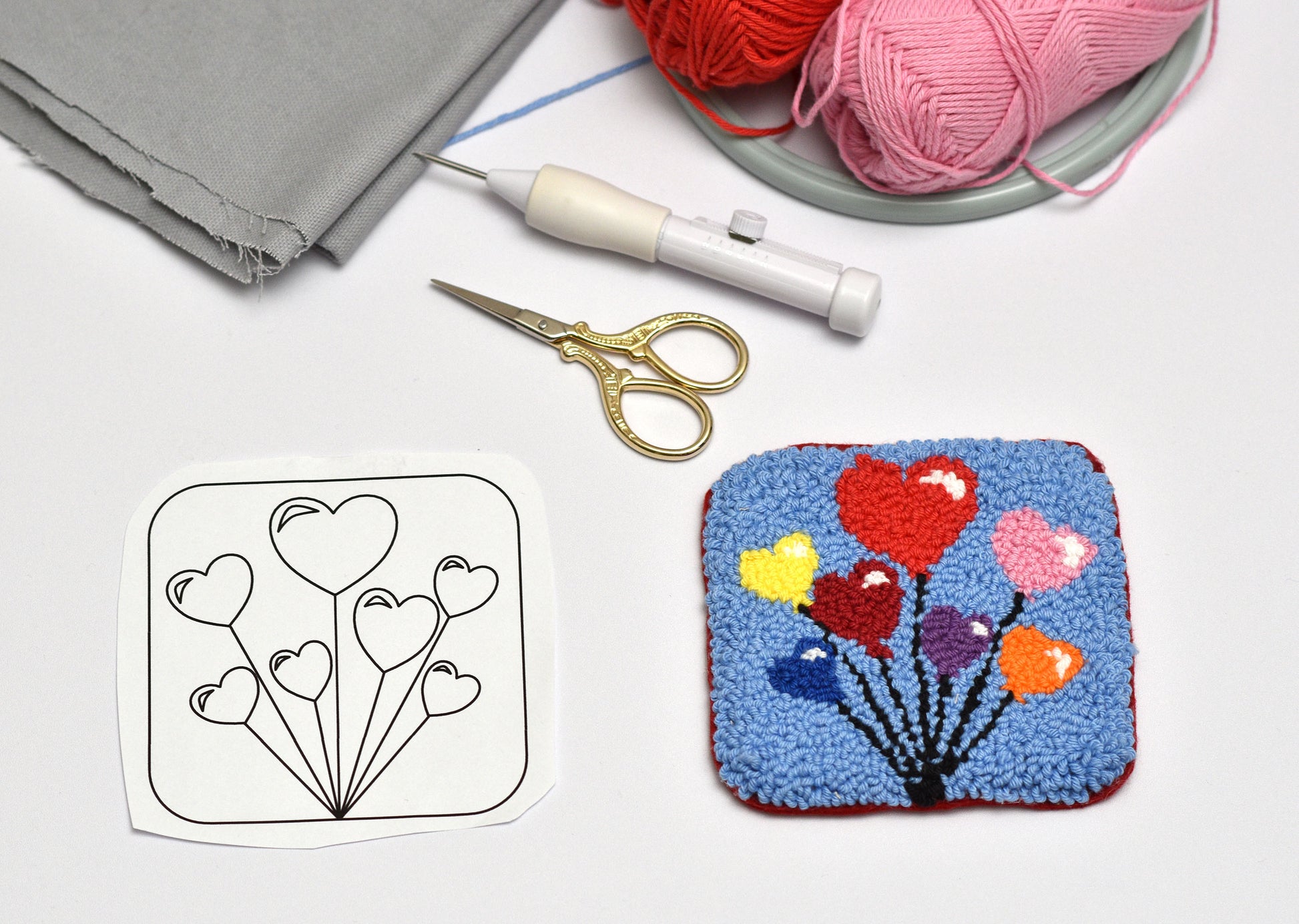 Crafting setup with a completed punch needle art of balloons and hearts, a template, scissors, and yarn.