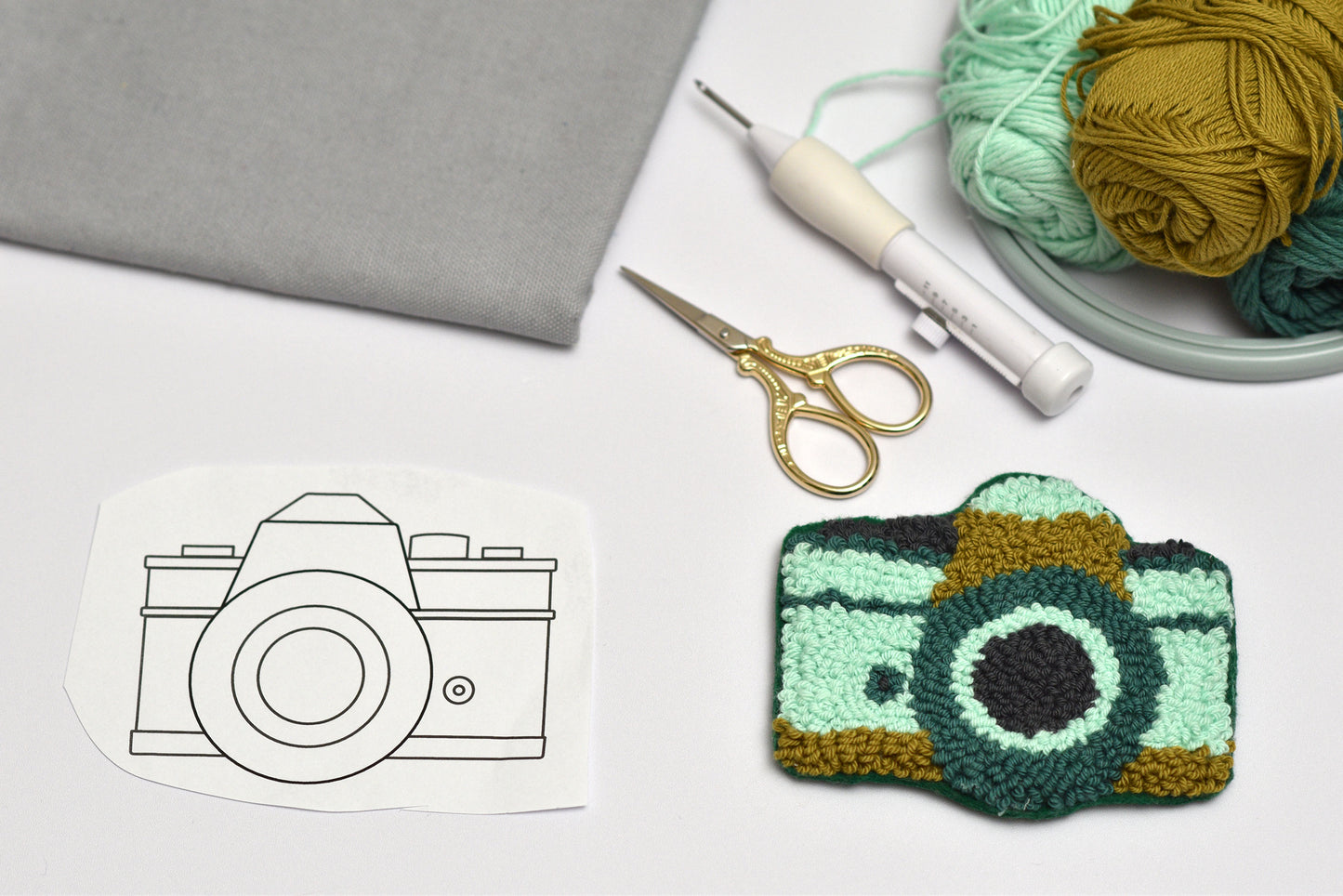 Embroidered coaster with camera design next to a coloring page and crafting supplies on a white surface