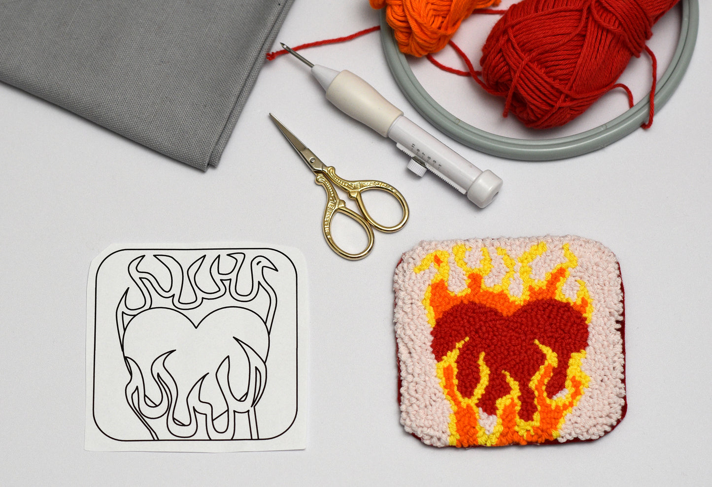Punch needled heart with flame design next to a black and white outline on a gray background.