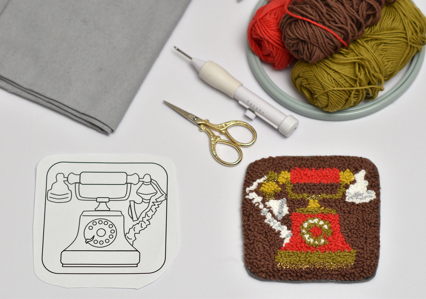 Punch needle phone design coaster next to a template and yarn on a gray surface
