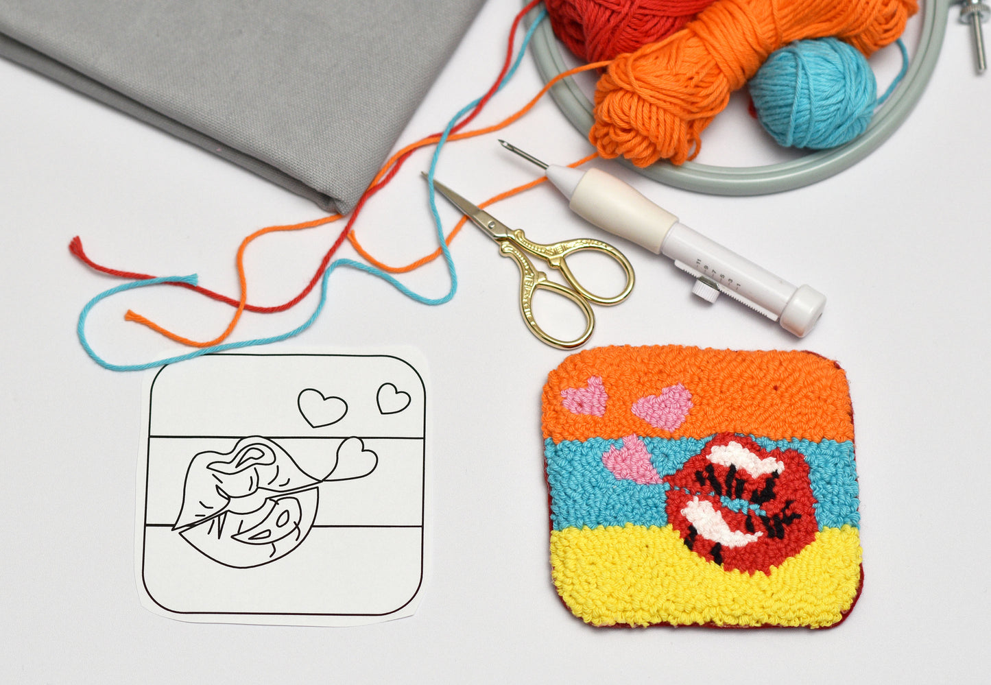 Embroidered coaster with colorful design next to yarn, punch needle hook, and scissors on a white surface.