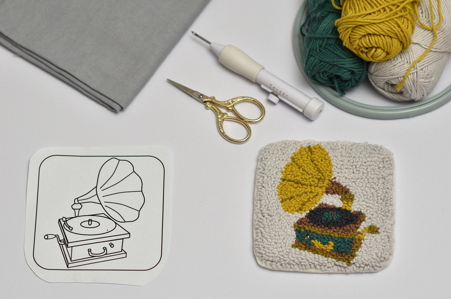 Embroidery hoop with yarn and a completed embroidered gramophone designed coaster on a flat surface.