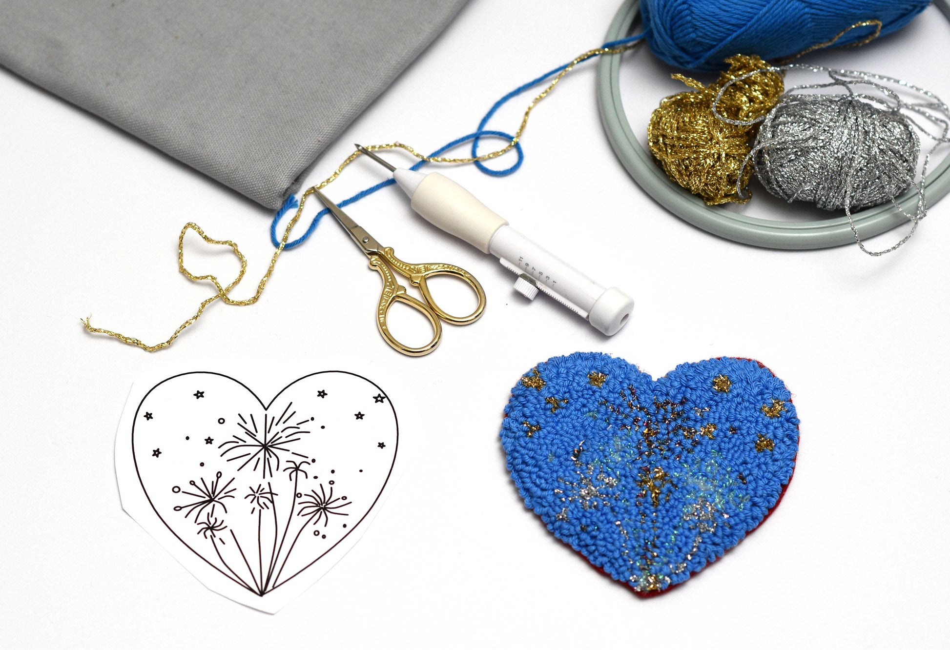 Blue embroidered heart with a template, scissors, and yarn on a white background