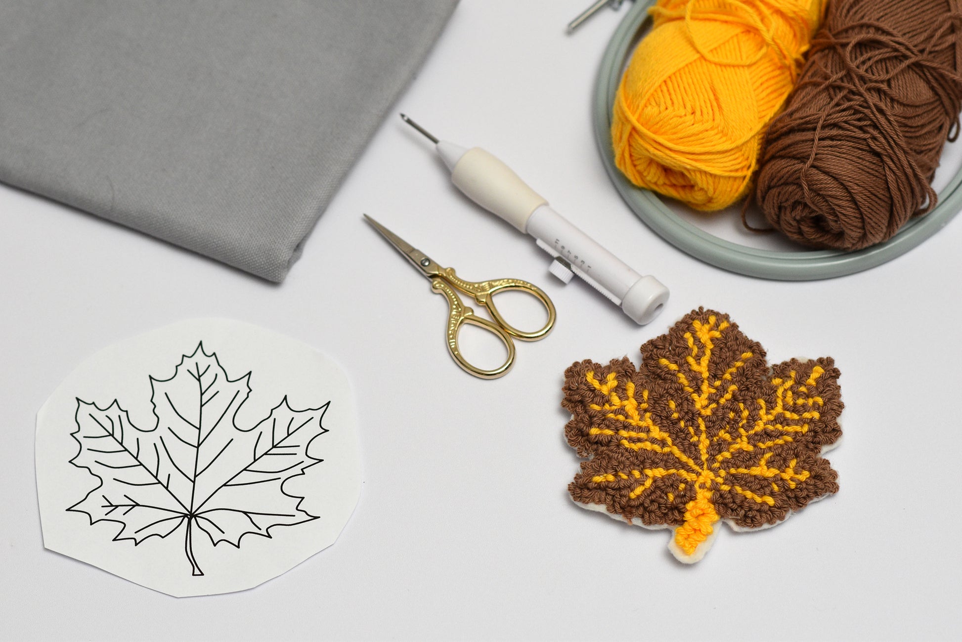 Punch needled leaf coaster with yarn and tools on a light surface