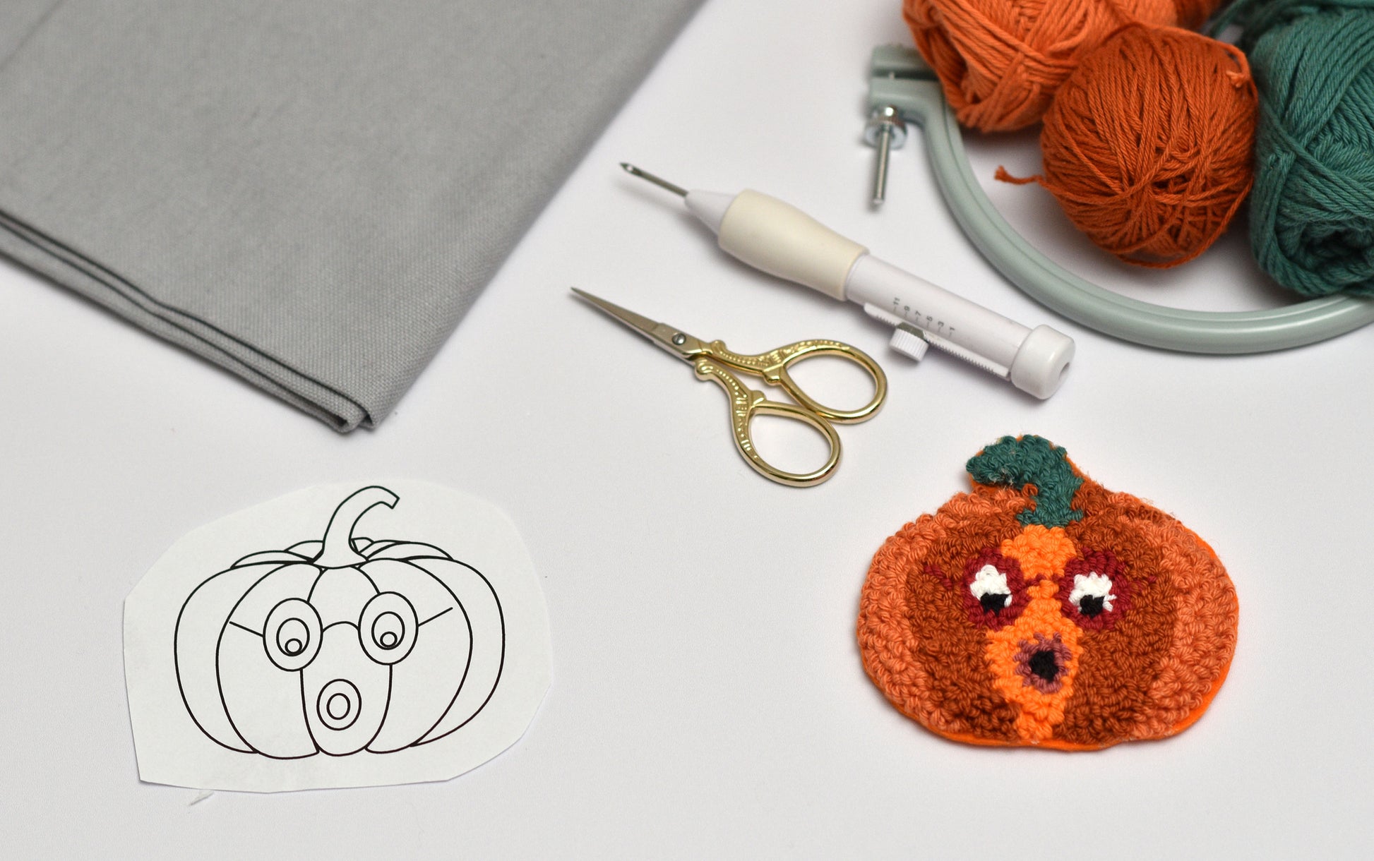 Punch needled pumpkin coaster with yarn, scissors, and a template on a white surface