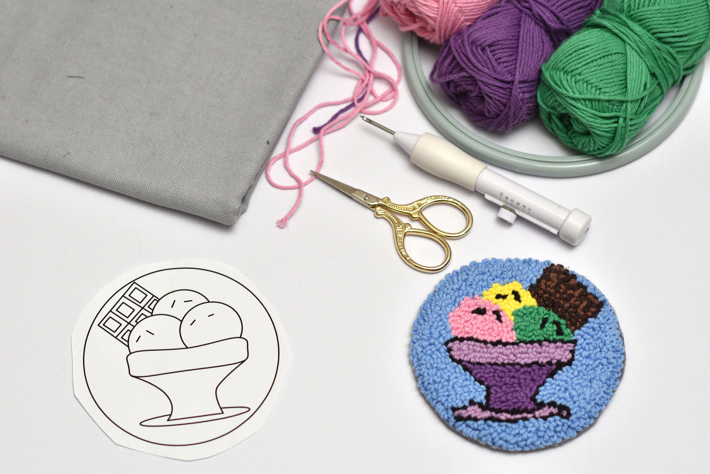 Punch needle rug with ice cream design next to yarn, scissors, and a needle on a white surface.
