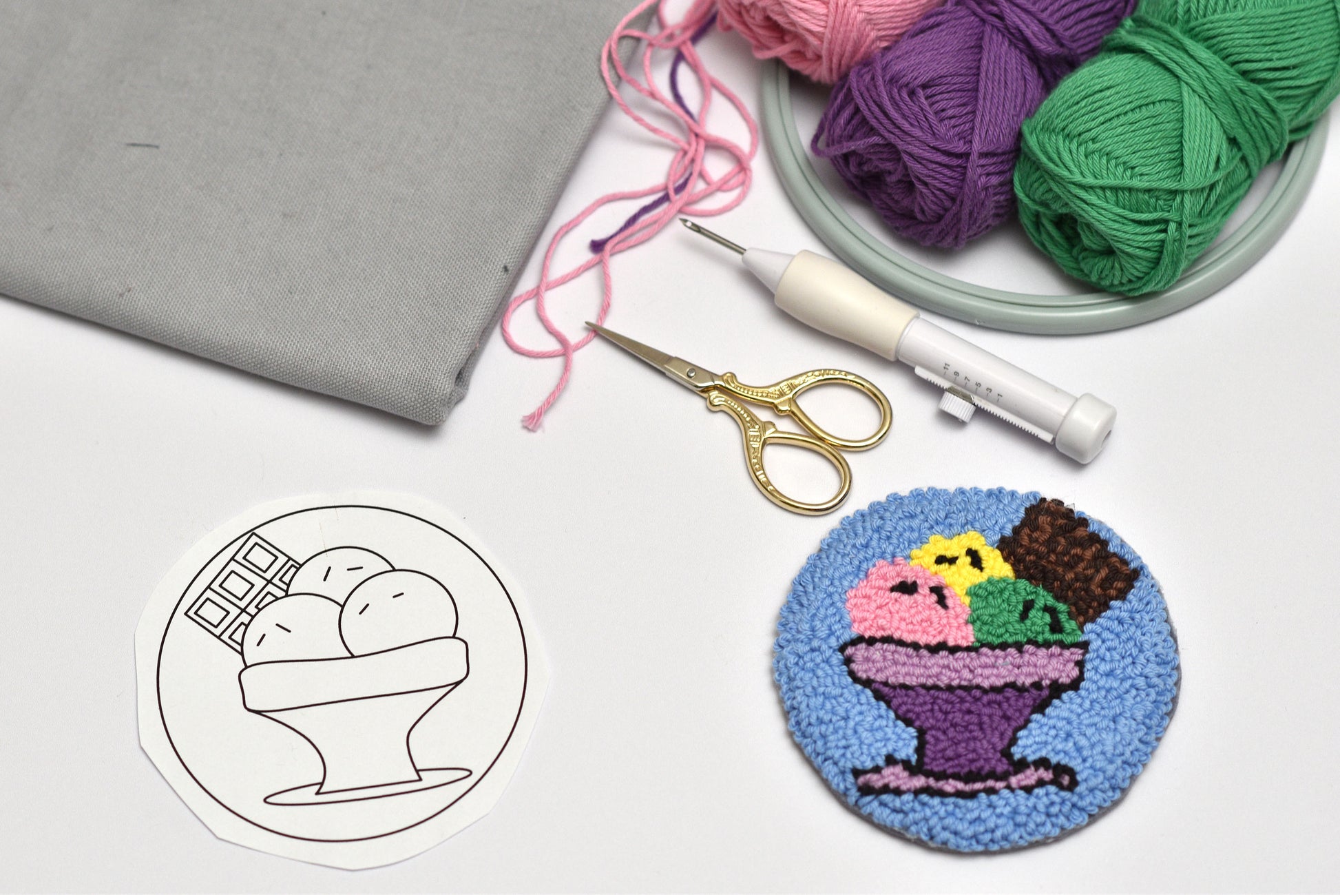 Punch needle rug with ice cream design next to yarn, scissors, and a needle on a white surface.