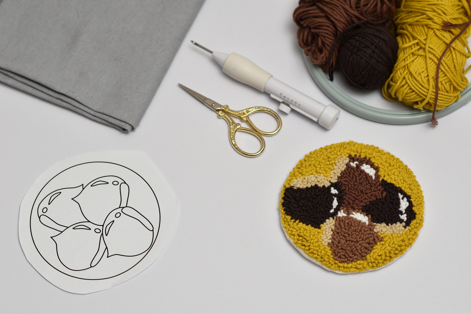 Round punch needle coaster with brown and yellow chestnuts, surrounded by yarn, scissors, and a template on a light gray surface.