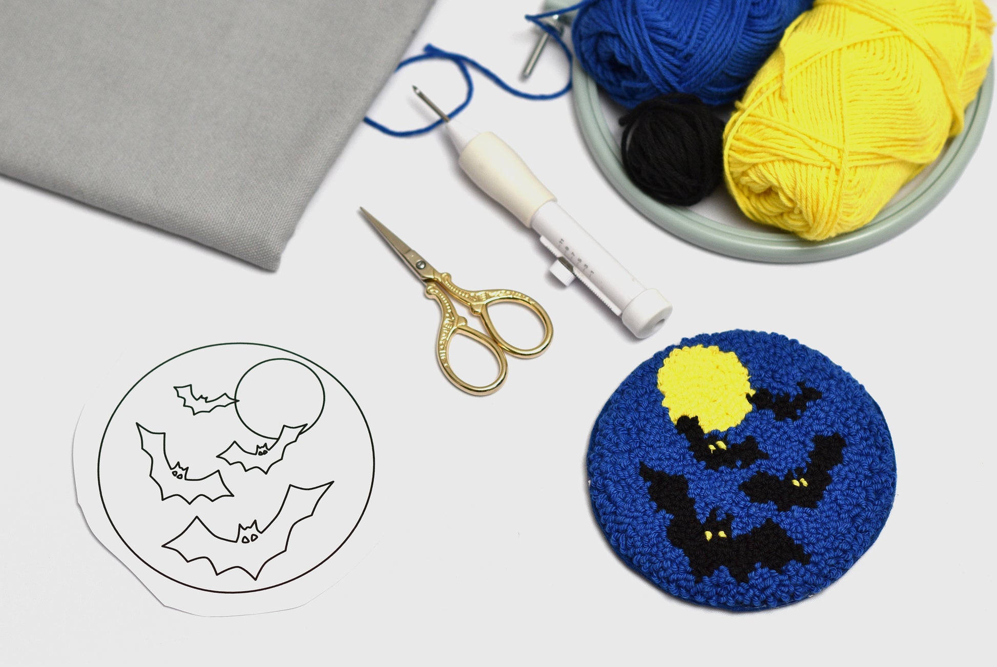 Embroidered coaster with bat design next to yarn and tools on a light surface
