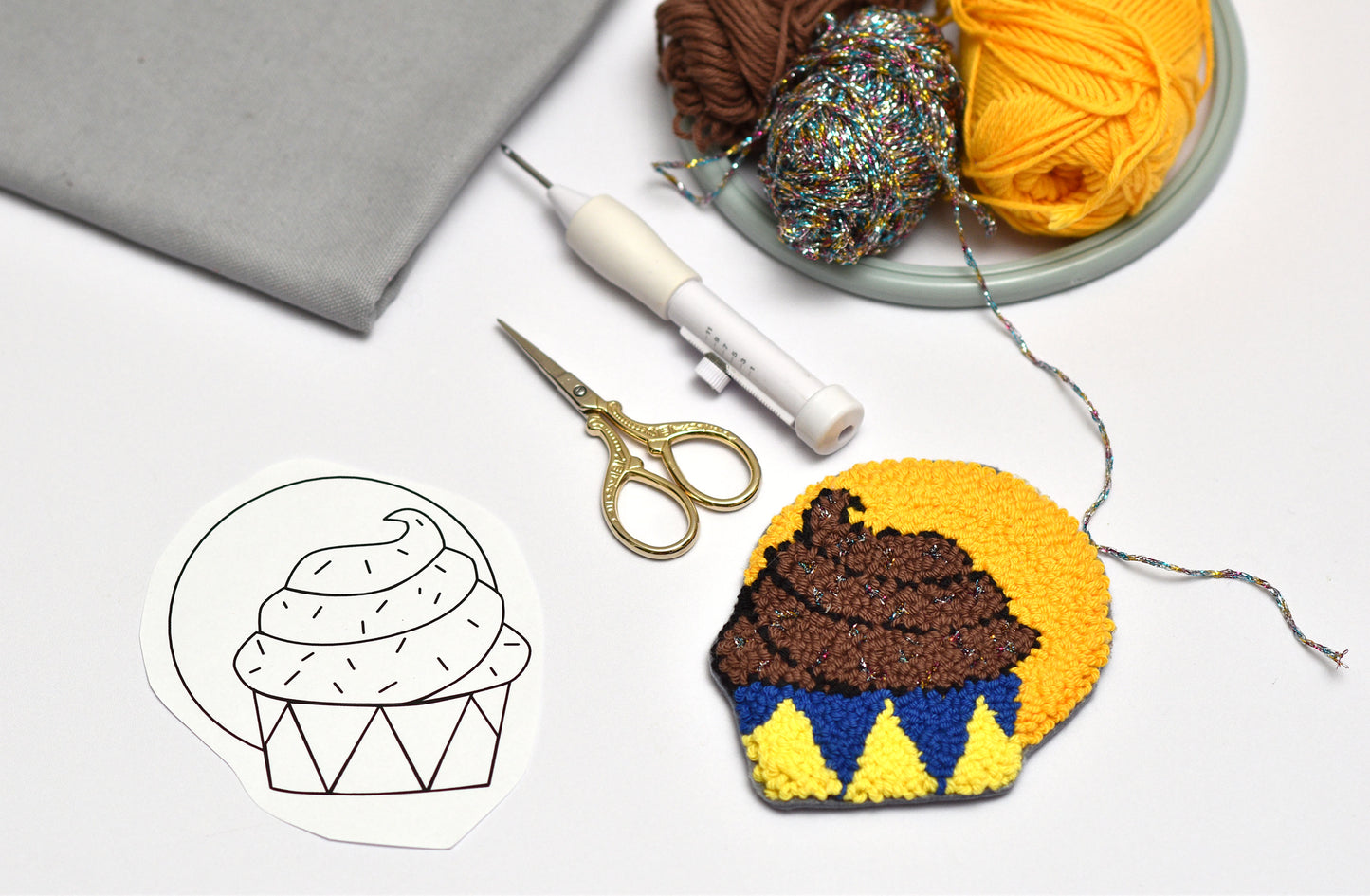 Embroidered cupcake coaster with yarn, scissors, and a pattern on a white background